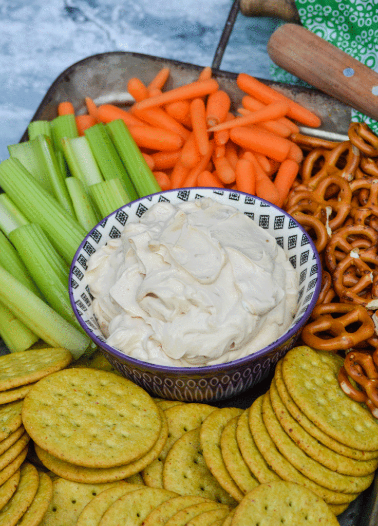 creamy french onion dip in a small purple bowl and surrounded by vegetables and crackers
