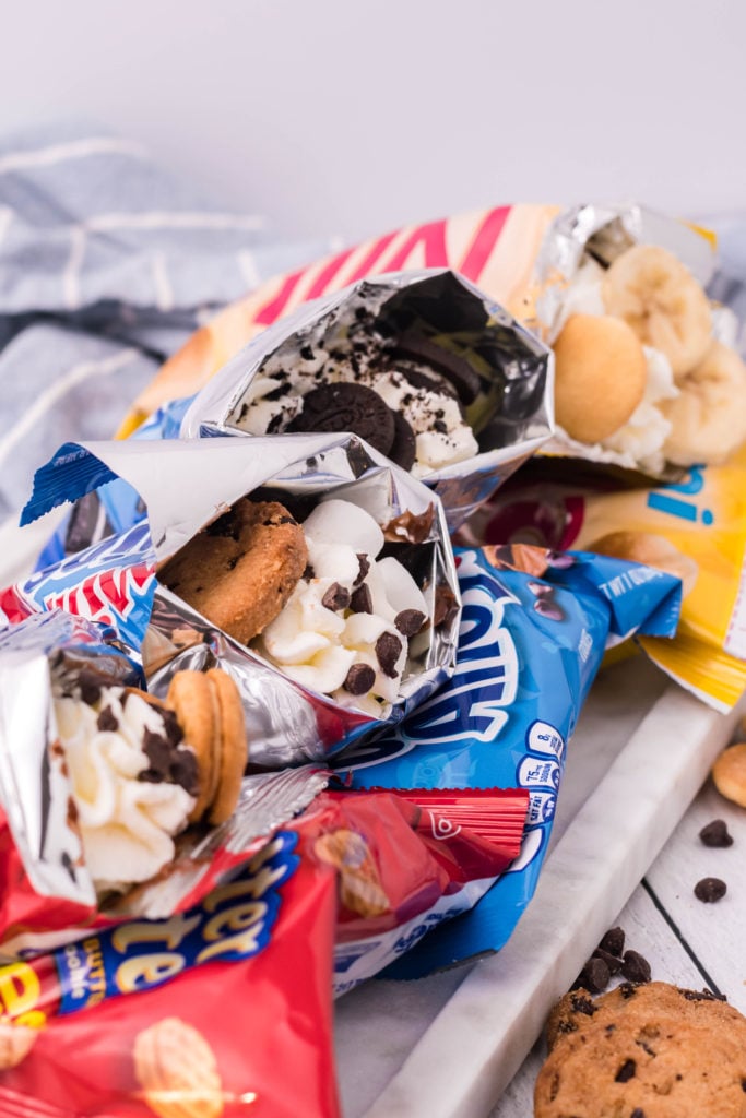 four different snack cookie bags stuffed as walking desserts and lined up on a marble platter