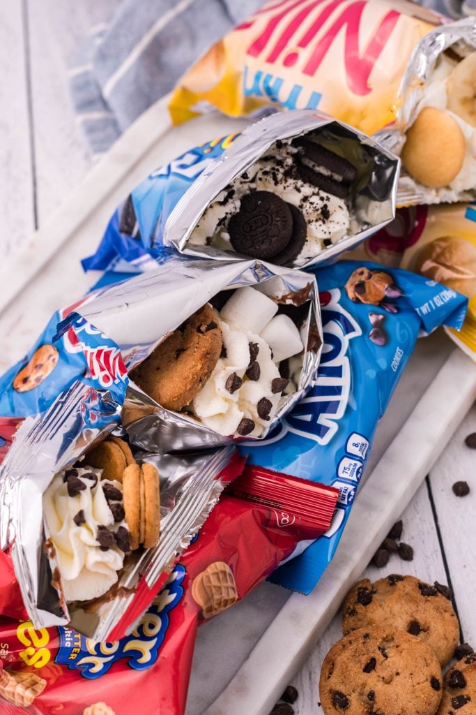 four different snack cookie bags stuffed as walking desserts and lined up on a marble platter