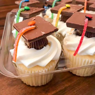 graduation cap cupcakes sitting in a clear plastic cupcake container