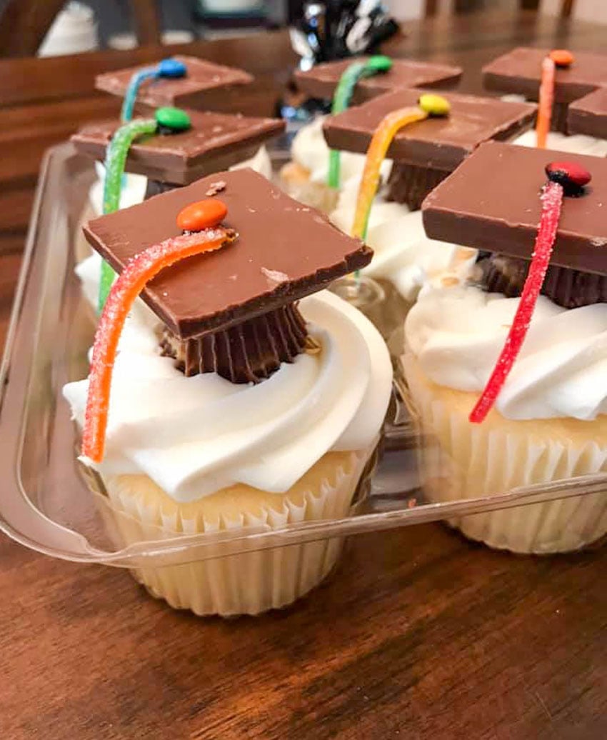 graduation cap cupcakes sitting in a clear plastic cupcake container