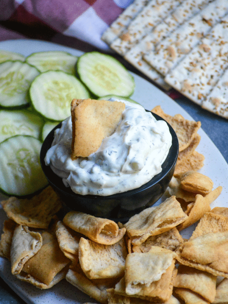 a small black bowl filled with homemade tzatziki dip surrounded by cucumber sliced and pita chips