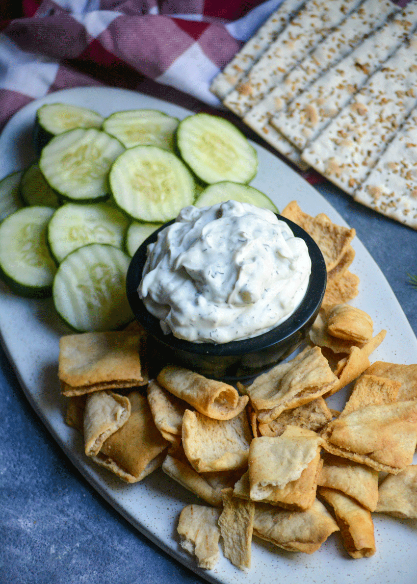 homemade tzatziki sauce in a back bowl surrounded by cucumber slices and pita chips