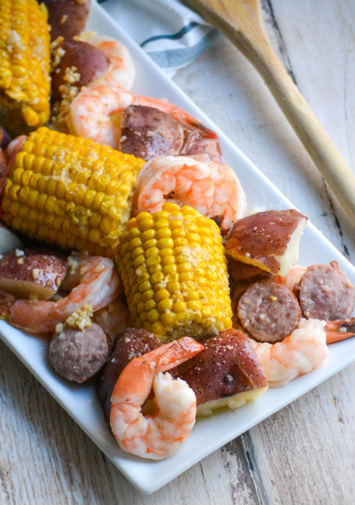 Instant pot shrimp boil shown on a rectangular white platter with a wooden spoon off to the side