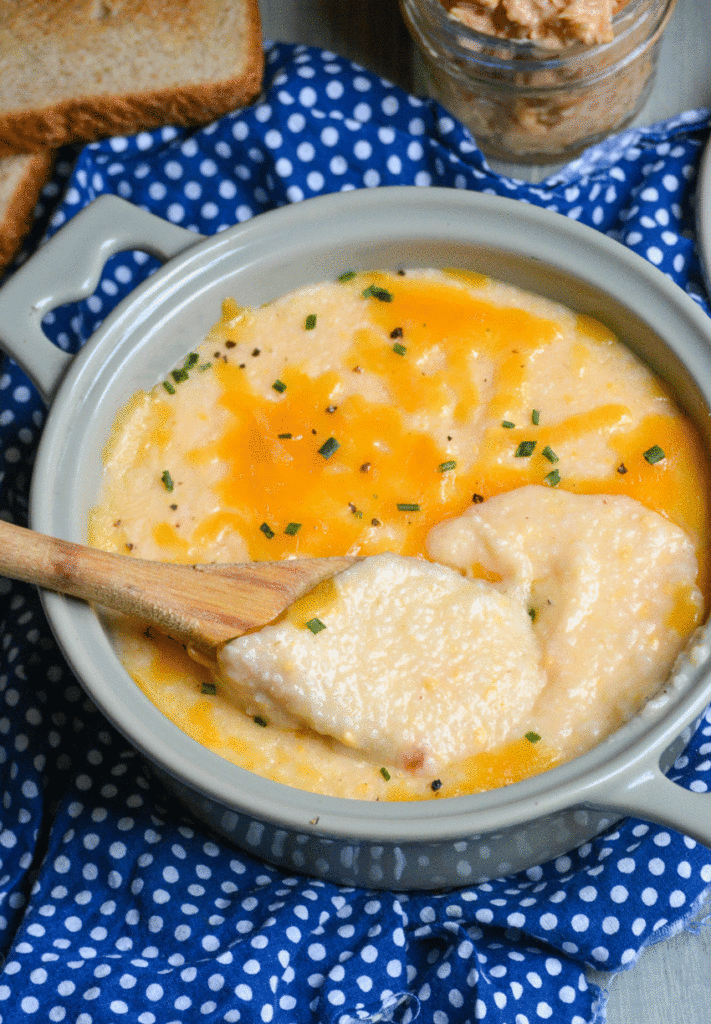 a wooden spoon shown scooping pimento cheese grits from a gray bowl