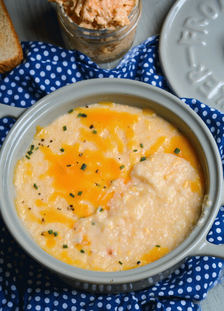 pimento cheese grits served in a gray crock with melted cheddar and chives sprinkled on top