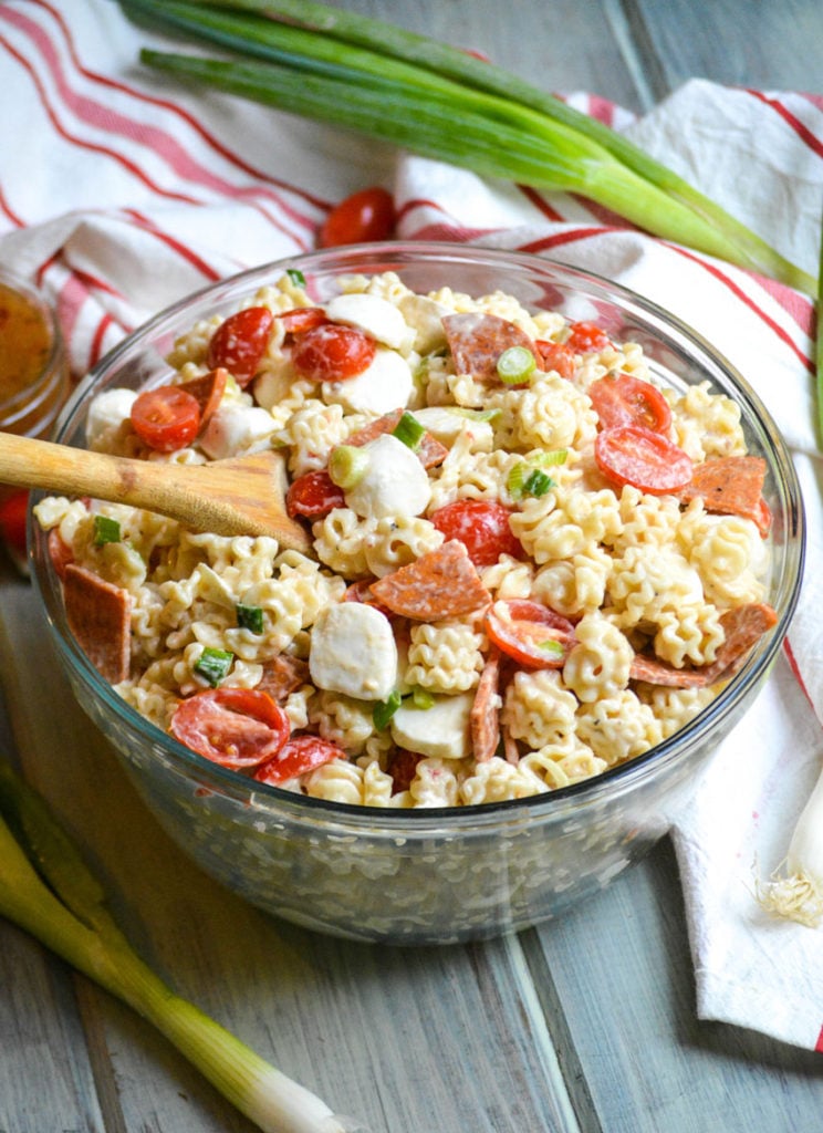a quick and easy pasta salad with pepperoni shown in a large glass bowl with a wooden spoon on the side