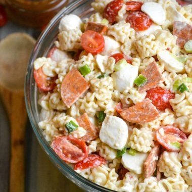a quick and easy pasta salad with pepperoni shown in a large glass bowl with a wooden spoon on the side