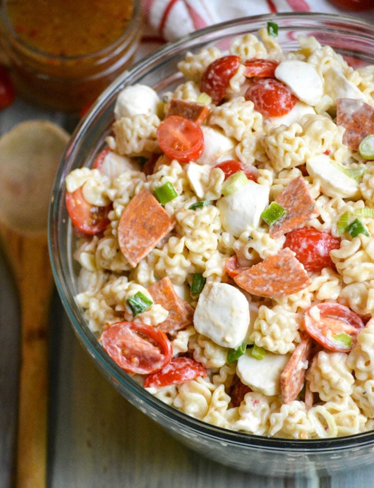 a quick and easy pasta salad with pepperoni shown in a large glass bowl with a wooden spoon on the side