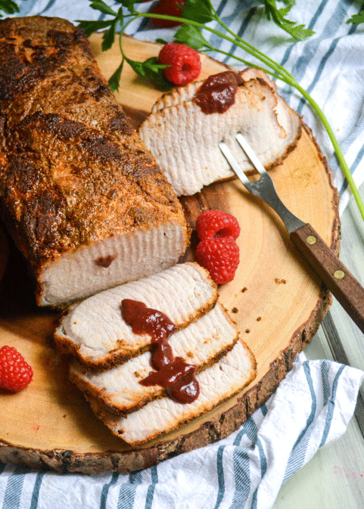 oven baked pork loin sliced and drizzled with some raspberry dijon barbecue sauce on a wooden cutting board