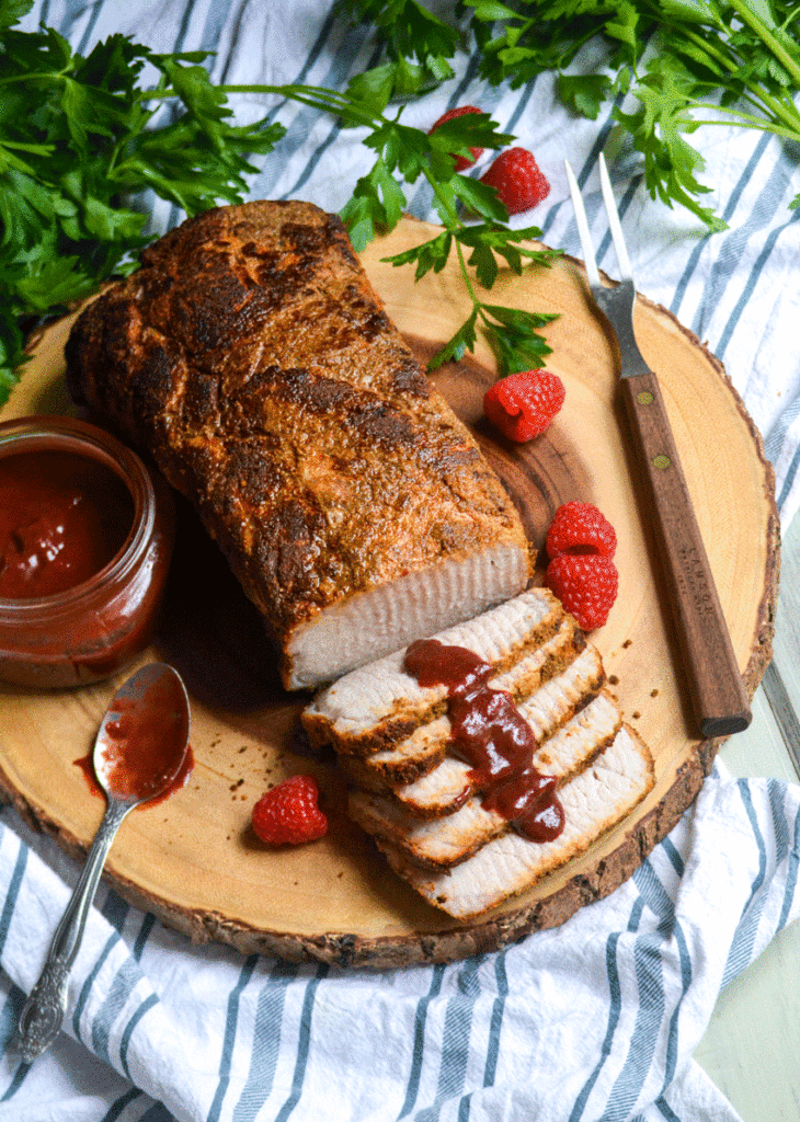 oven roasted pork loin sliced and drizzled with some raspberry dijon barbecue sauce on a wooden cutting board