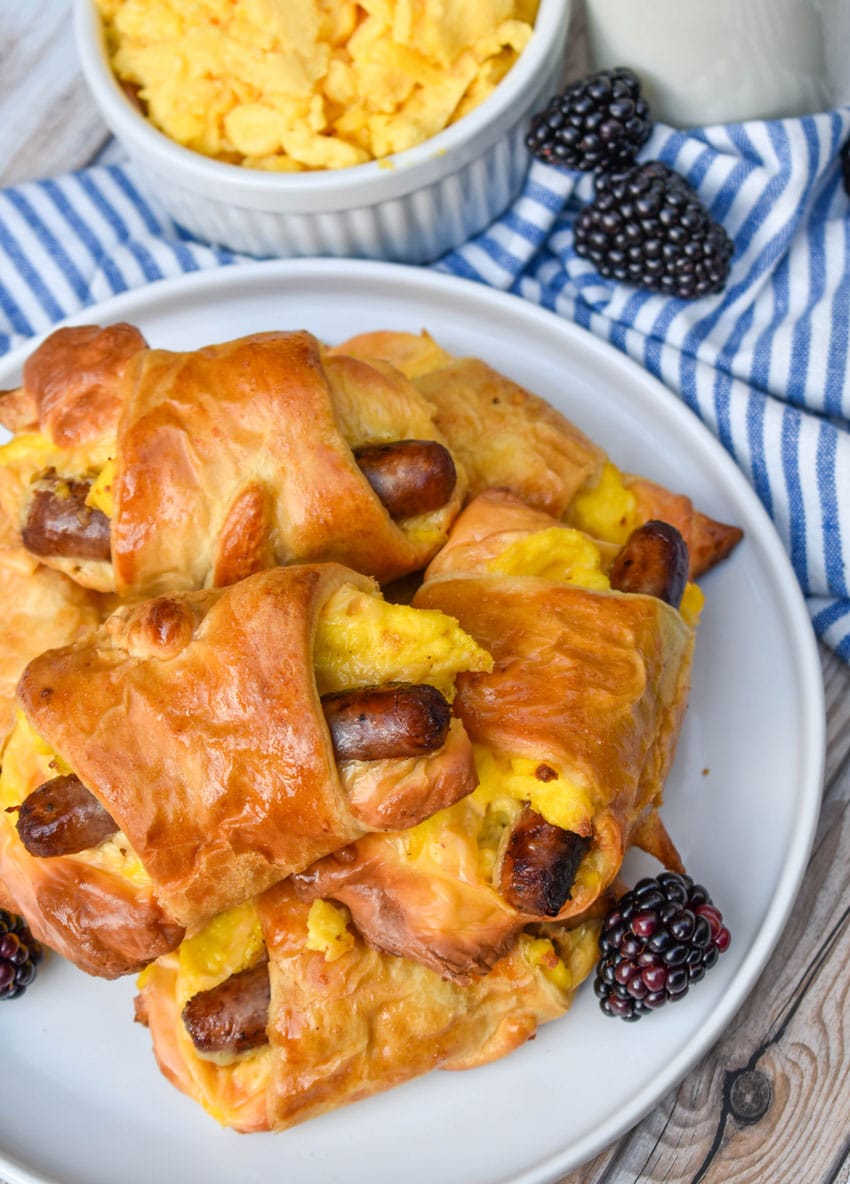 SAUSAGE EGG AND CHEESE BREAKFAST CRESCENT ROLLS STACKED ON A WHITE PLATE WITH FRESH BLACKBERRIES ON THE SIDE