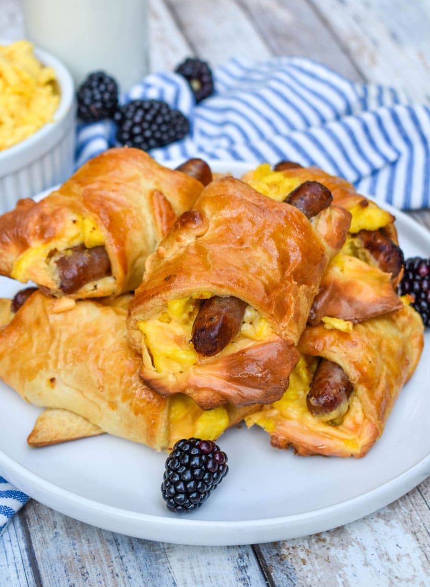 SAUSAGE EGG AND CHEESE BREAKFAST CRESCENT ROLLS STACKED ON A WHITE PLATE WITH FRESH BLACKBERRIES ON THE SIDE