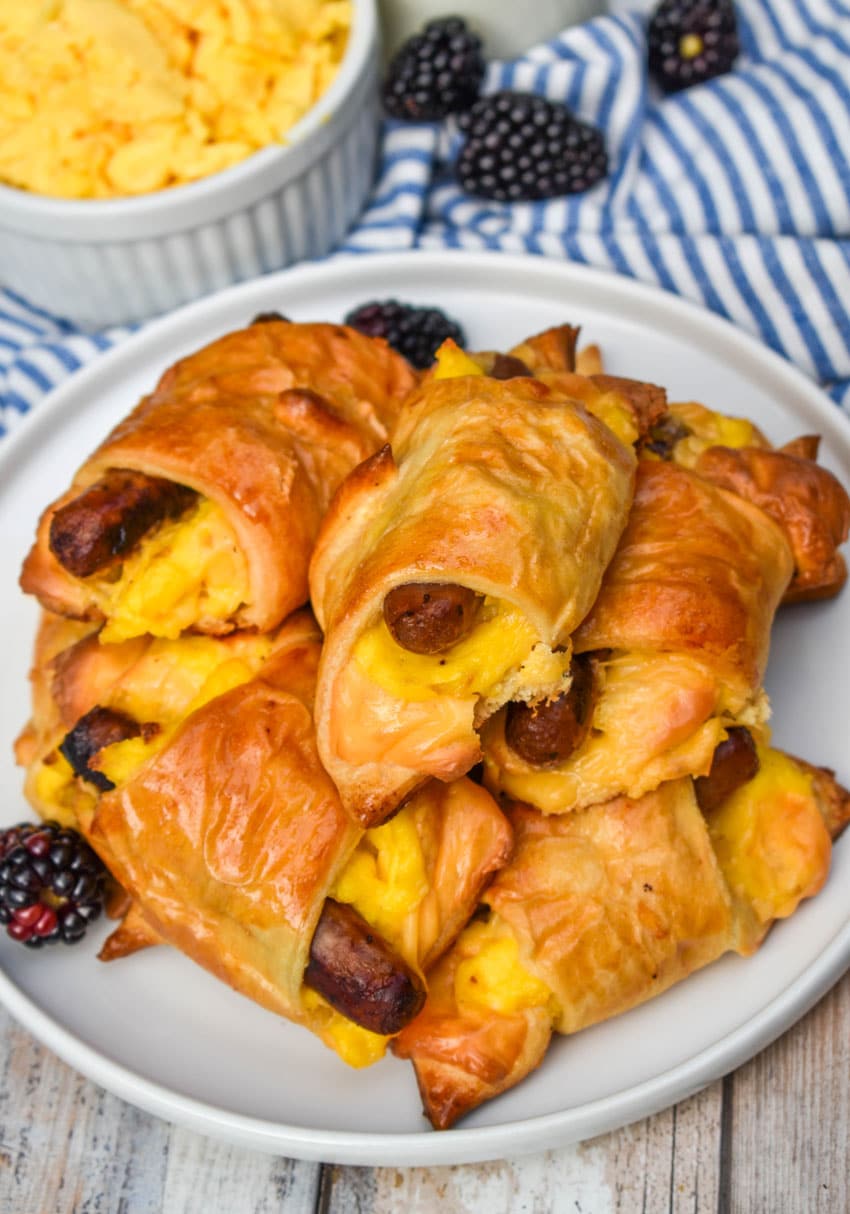 SAUSAGE EGG AND CHEESE BREAKFAST CRESCENT ROLLS STACKED ON A WHITE PLATE WITH FRESH BLACKBERRIES ON THE SIDE