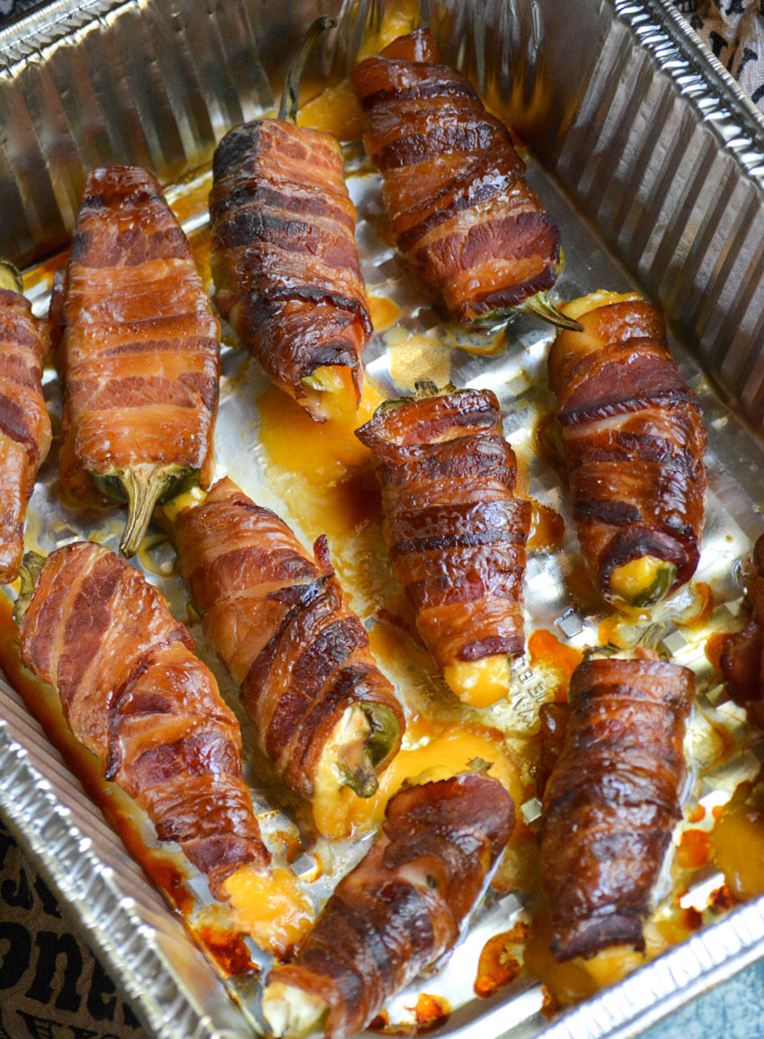 bacon wrapped smoked jalapeno poppers shown in a disposable aluminum tray