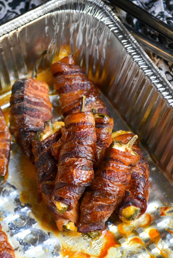 bacon wrapped smoked jalapeno poppers piled up in an aluminum tray