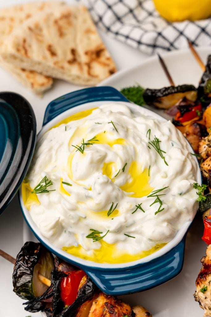 homemade Greek tzatziki sauce in a blue ramekin topped with a drizzle of olive oil and fresh herbs