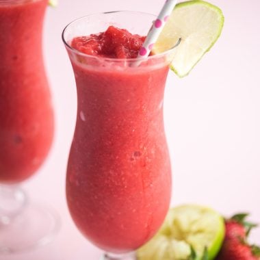 two strawberry daiquiris in glass jars garnished with lime slices and paper straws
