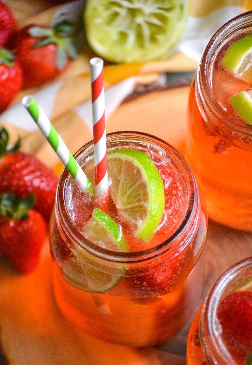 a glass of strawberry limeade shown with fresh fruit garnish and striped paper straws