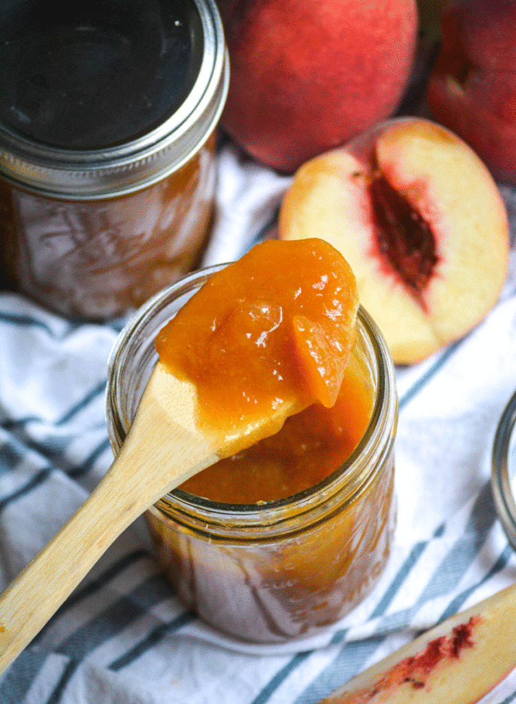 Instant pot peach jam on a wooden spoon resting on a glass mason jar