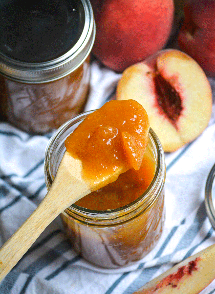 Instant pot peach jam on a wooden spoon resting on a glass mason jar