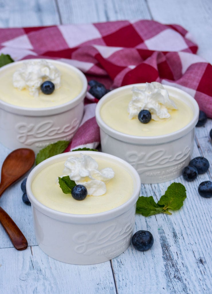 lemon cheesecake mousse shown in three white ramekins with whipped cream, blueberries, and mint leaves for garnish