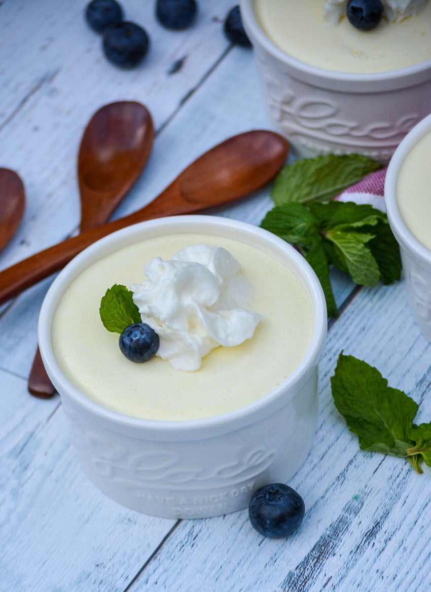 lemon cheesecake mouse in a white ramekin topped with a dollop of whipped cream a fresh blueberry and small mint leaf