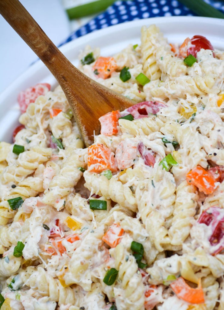 seafood pasta salad served in a white bowl with a wooden spoon stuck in the center