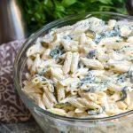 spinach dip pasta salad in a large glass bowl with fresh herbs in the background