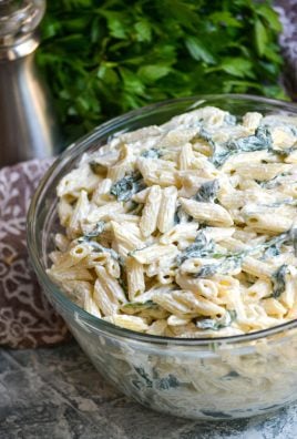 spinach dip pasta salad in a large glass bowl with fresh herbs in the background