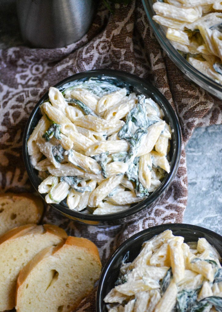 spinach dip pasta salad served in a small black bowl with baguette slices on the side
