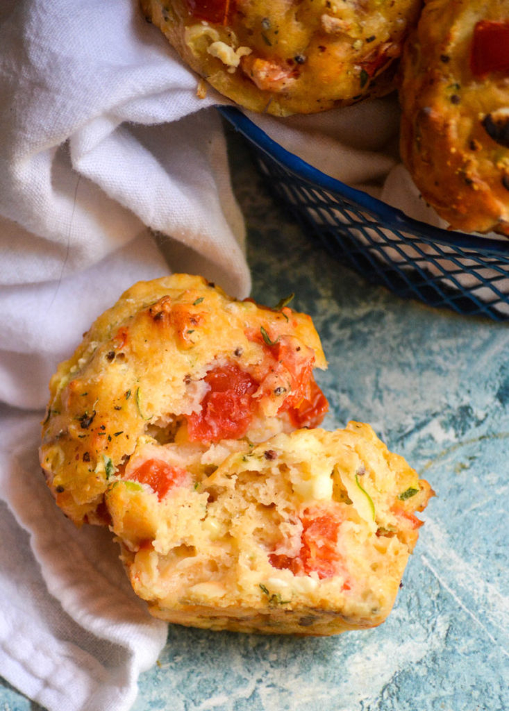 a single tomato zucchini feta muffin broken open to reveal the baked inside