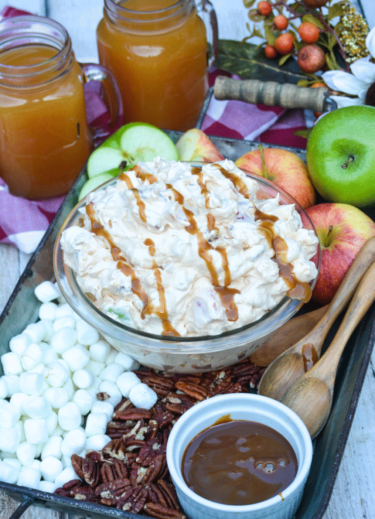 a bowl of caramel apple fluff salad on a tray with wooden spoons and ripe apples