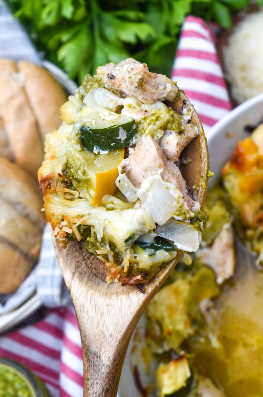 a wooden spoon holding up a scoop of cheesy pesto chicken and squash