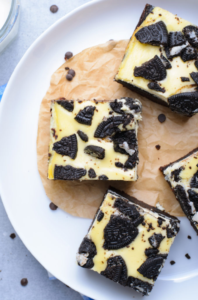 oreo cheesecake brownie squares shown on a parchment paper lined white plate