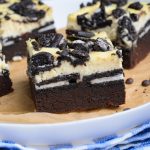 oreo cheesecake brownies on a parchment paper lined white plate