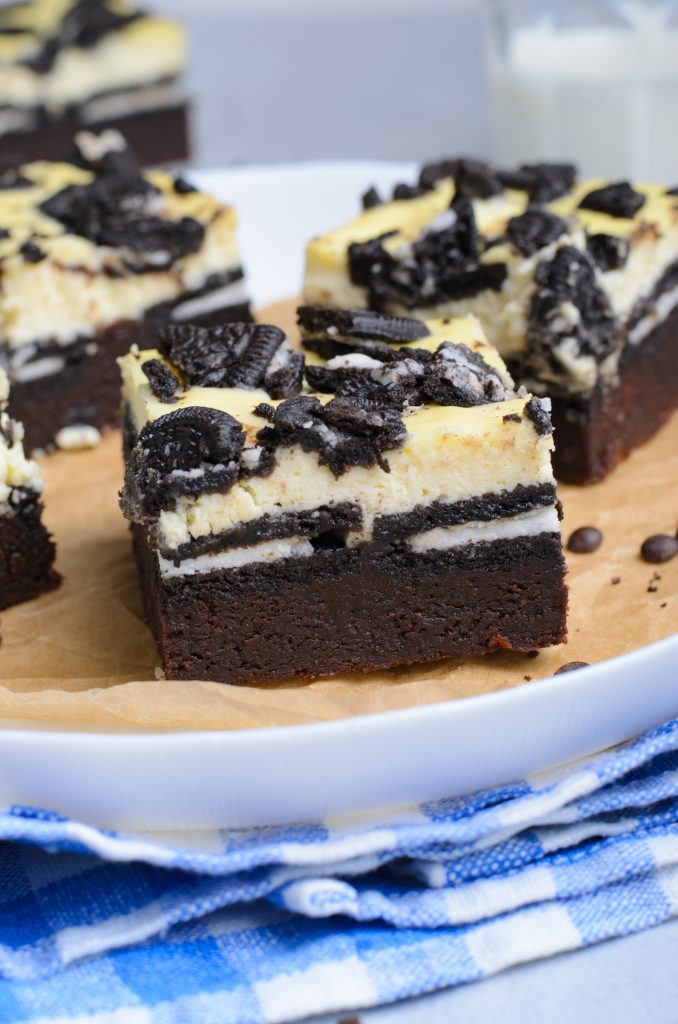 oreo cheesecake brownies on a parchment paper lined white plate