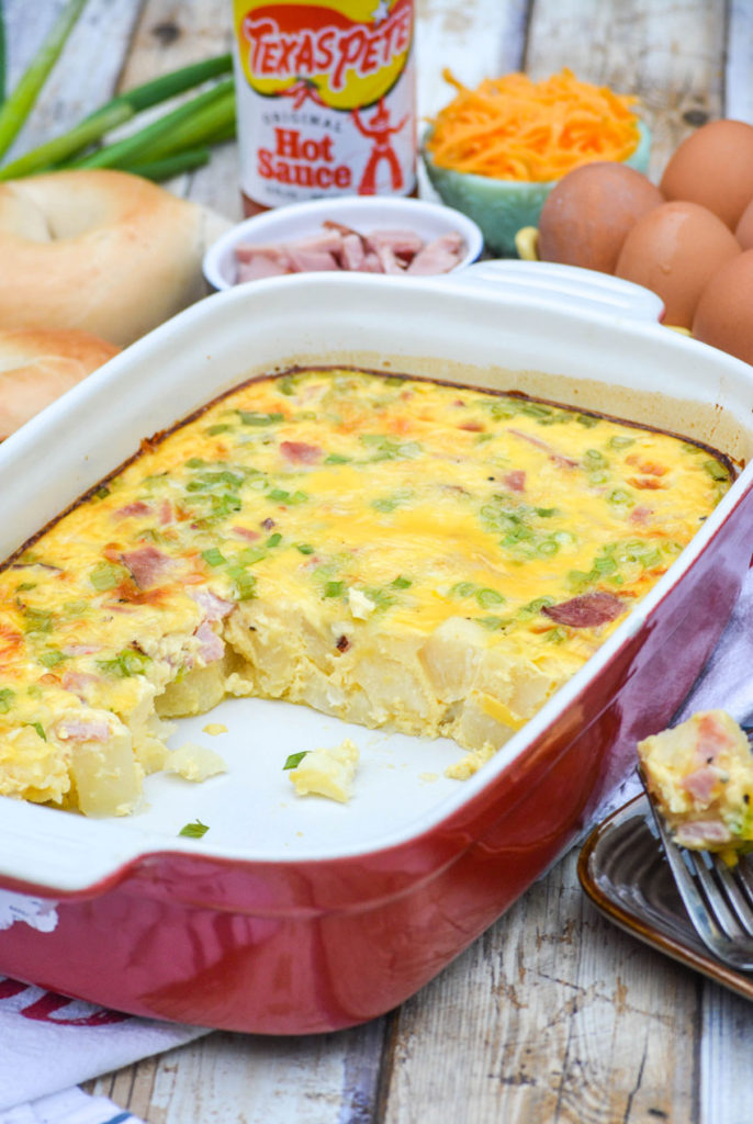 farmer's breakfast casserole in a casserole dish surrounded by ingredients and cut up to reveal the center