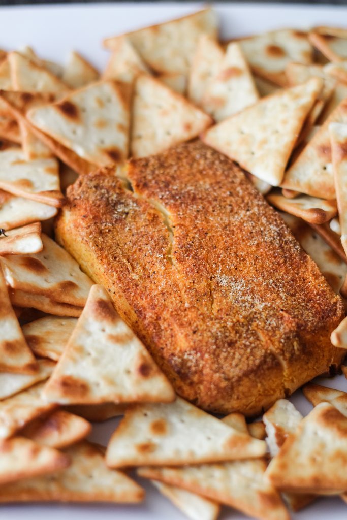 a bar of smoked cream cheese on a white plate surrounded by pita crackers