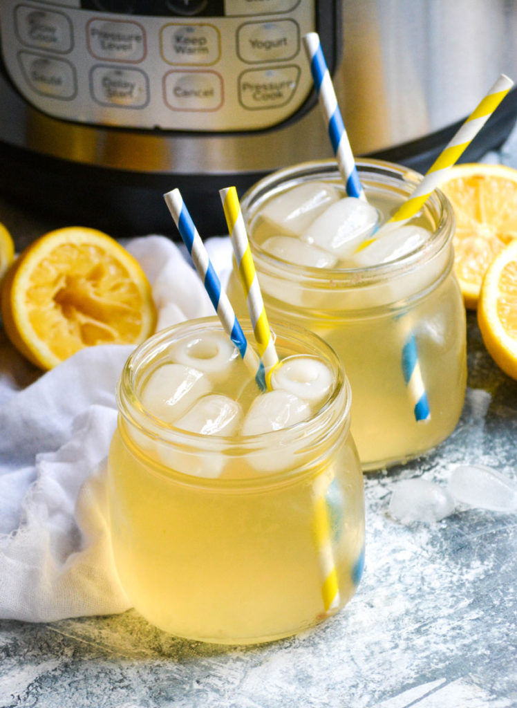 Instant pot lemonade shown in a glass jar with ice cubes and two striped paper straws