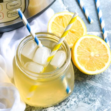 Instant pot lemonade shown in a glass jar with ice cubes and two striped paper straws