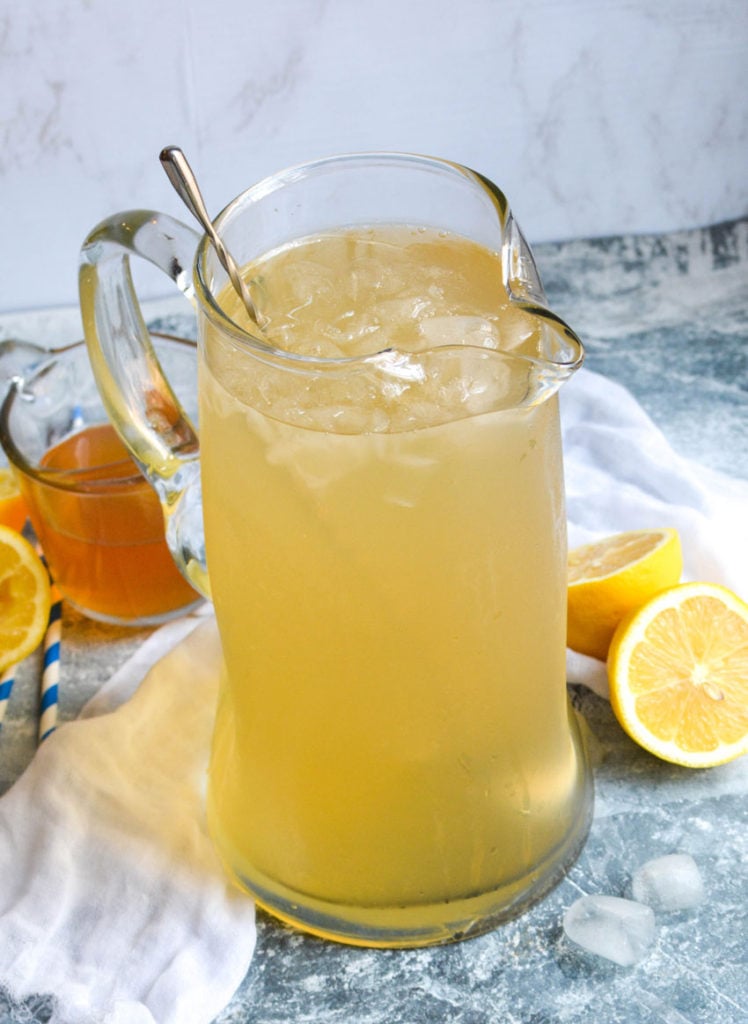 a glass pitcher full of instant pot lemonade over ice with a metal stir stick in it