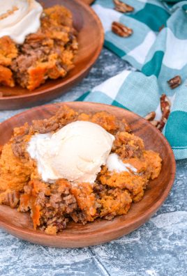 pumpkin pecan dump cake on wooden plates topped with a scoop of melting vanilla ice cream
