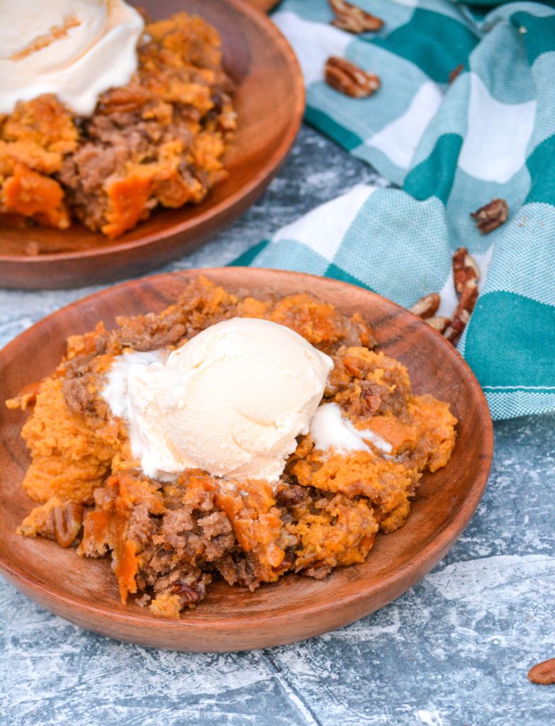 pumpkin pecan dump cake on wooden plates topped with a scoop of melting vanilla ice cream