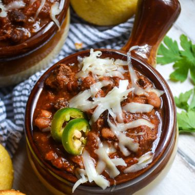 a brown crock style bowl filled with smoked brisket chili garnished with melted cheese and jalapeno slices