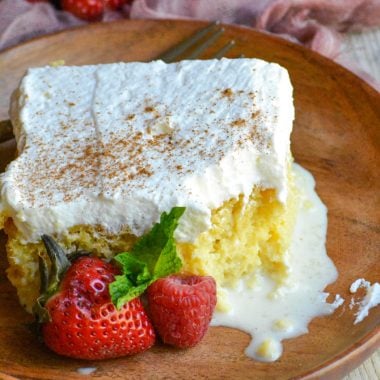a slice of tres leches cake on a small wooden plate with fresh berries