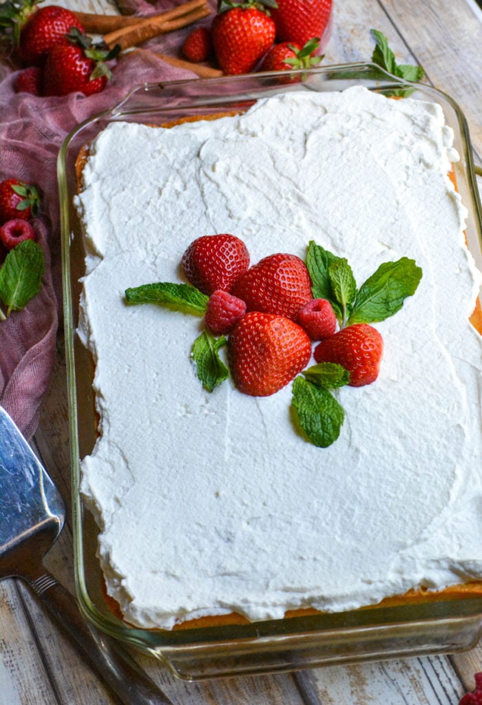 a tres leches cake baked in a 9x13 inch glass dish and topped with fresh berries & mint leaves