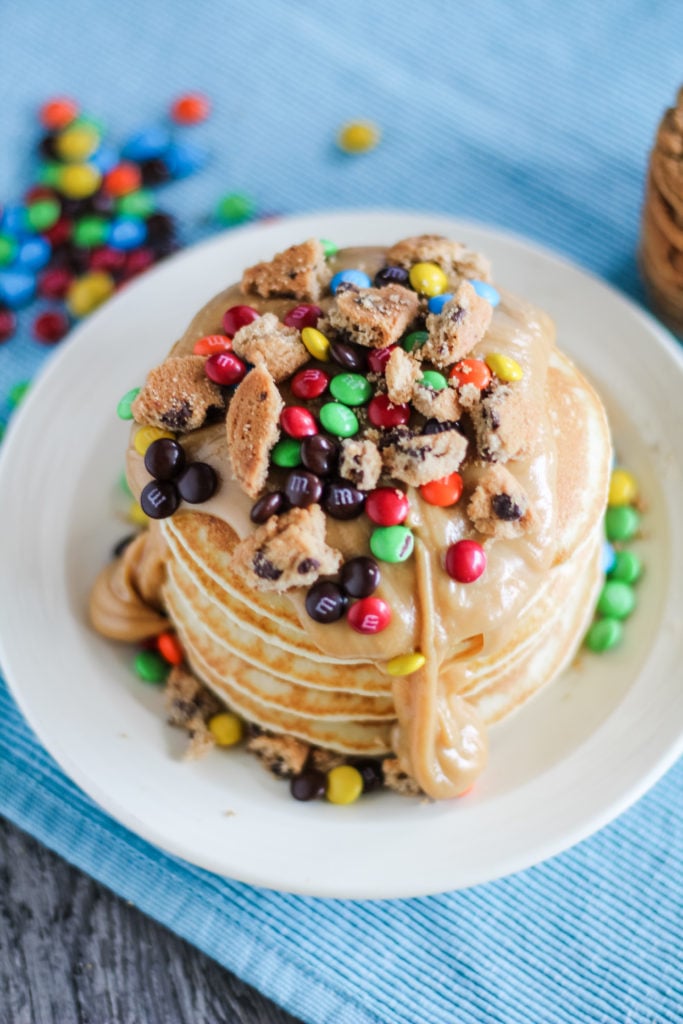 an overhead view of a stack of monster cookie pancakes on a white plate