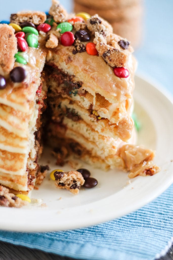 a stack of monster cookie pancakes with a sliced wedge removed to reveal the inside look of cakes