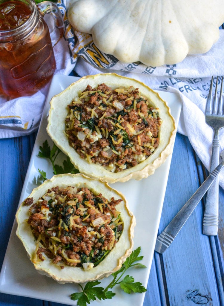two stuffed pattypan squash on a white platter with green herbs on the side